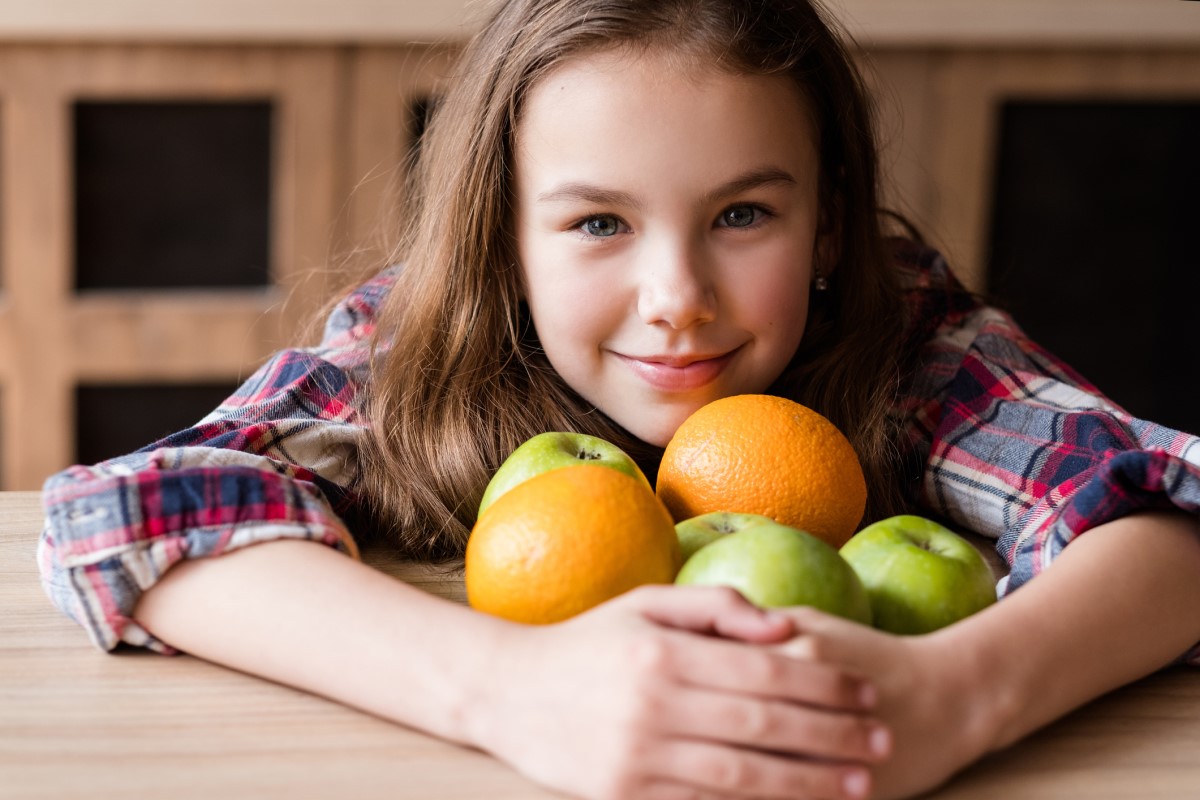 Vitamina C, în fructe, un copil care ține portocale și mere în brațe