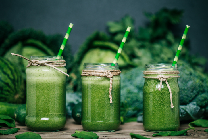 Smoothie de legume verzi, trei pahare, cu varză, broccoli și mazăre în fundal